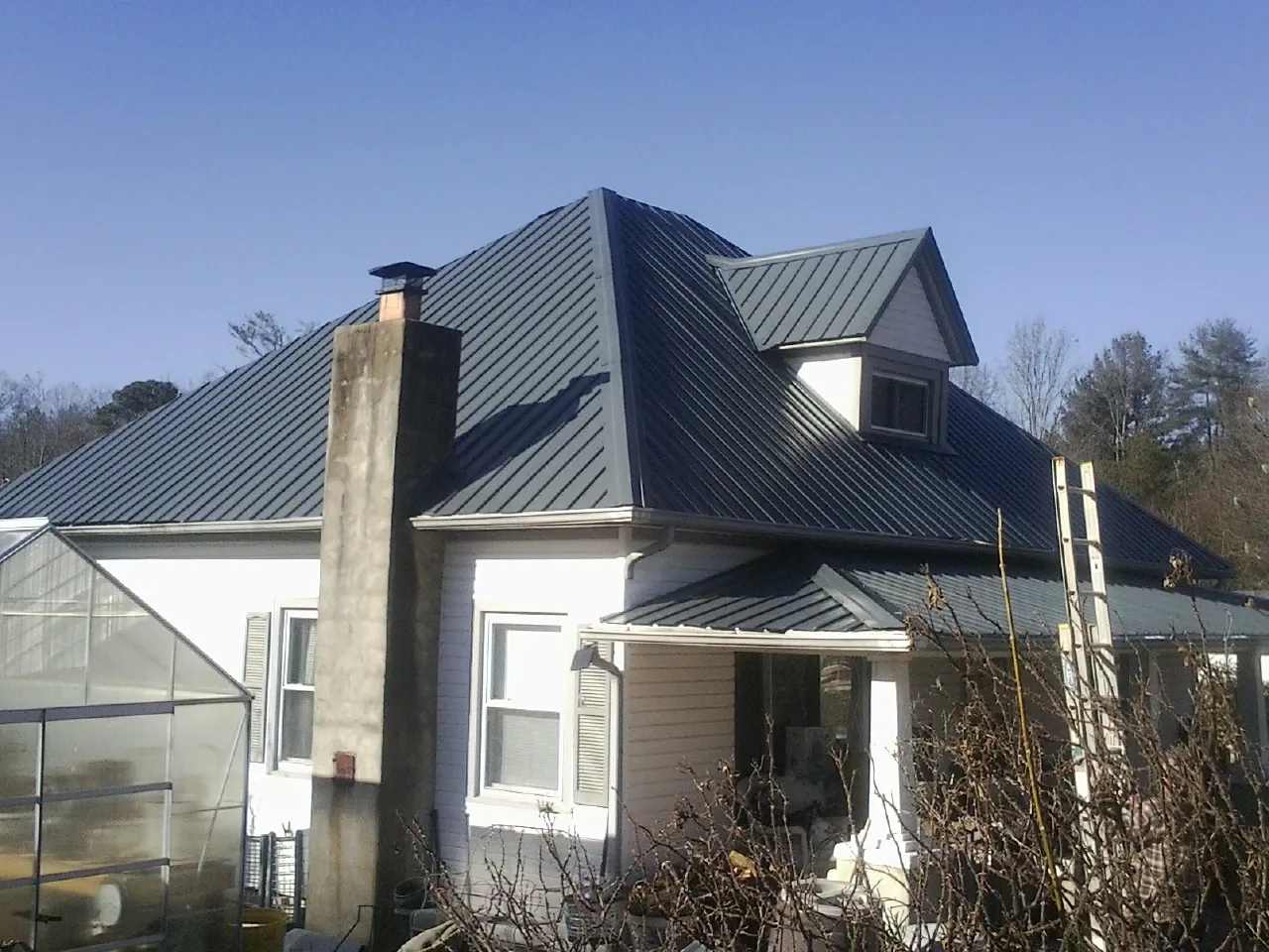 Dark blue standing seam metal roof on a white farmhouse with dormer — Slate & Tile Roof Repair by Roofing Brothers in Selmer