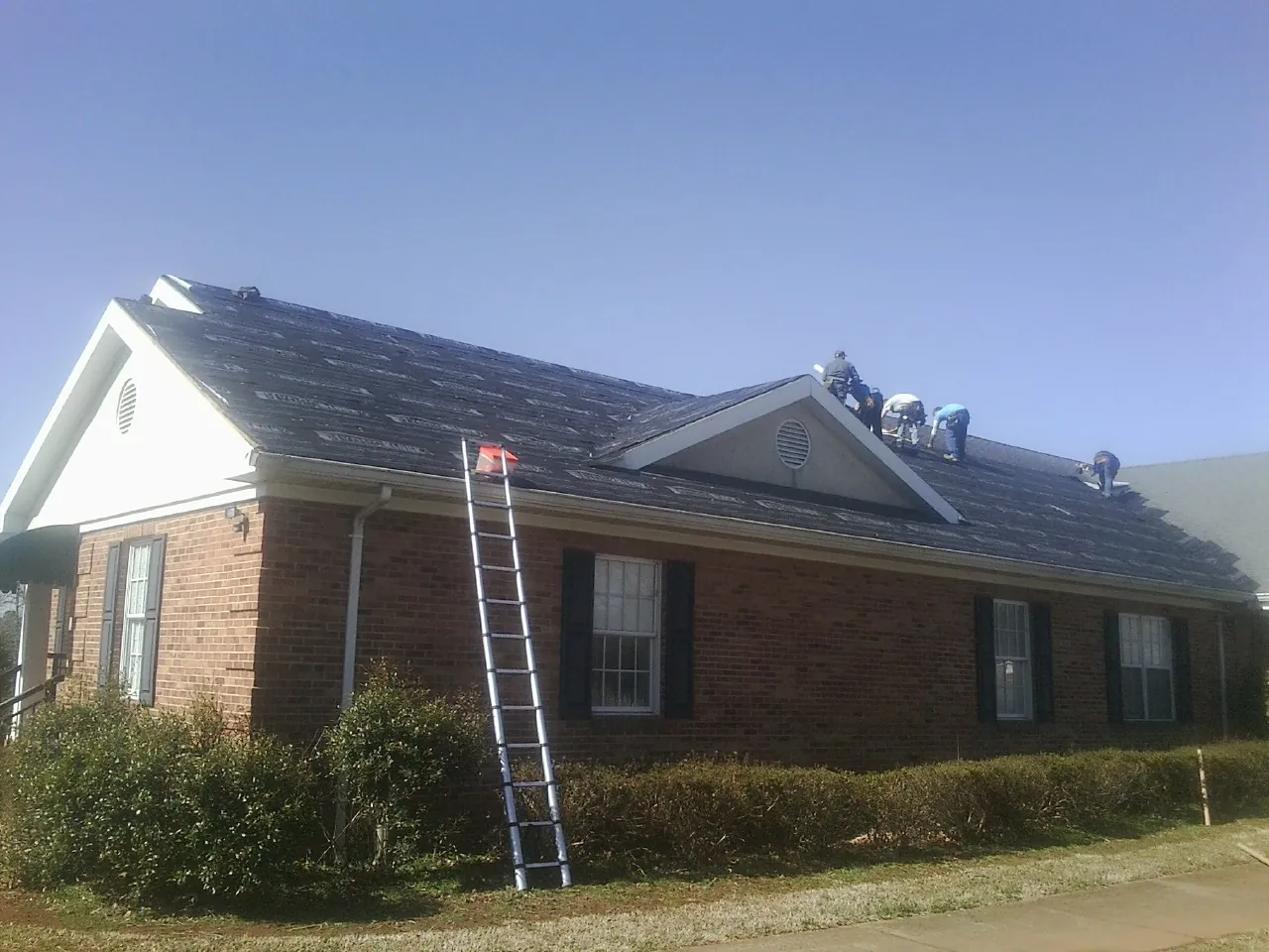 Crew tearing shingles off a brick ranch roof with a ladder set — Emergency Roof Repair work by our crew in Selmer