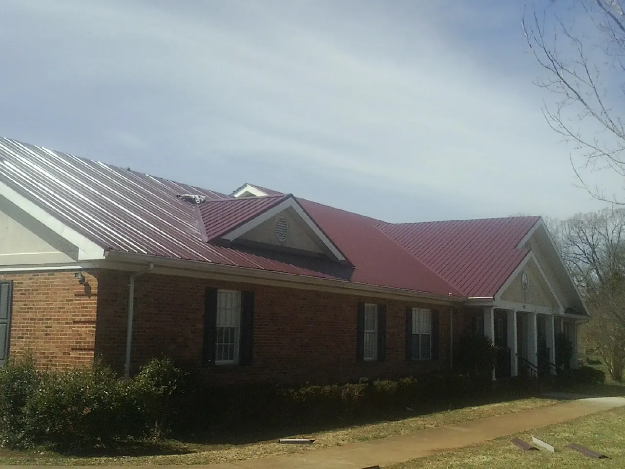 Red metal roof with gabled entries on a long brick building, from a Hail Damage Roof Repair job in Selmer