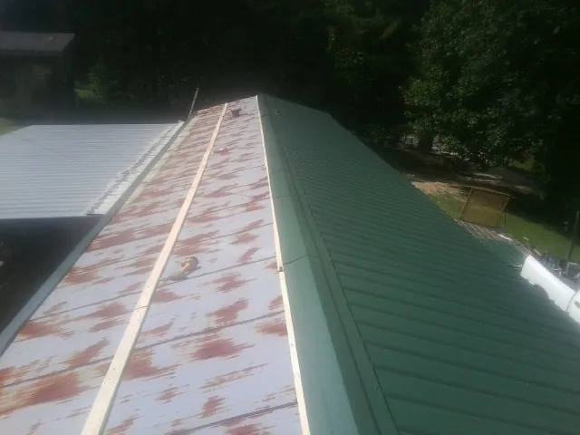 Old rusted panels beside newly installed green metal roofing — Wind Damage Roof Repair by Roofing Brothers in Selmer