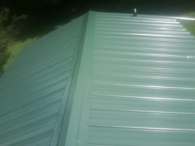 New green metal panels meeting at the ridge of a roof — Flat Roof Repair work by our crew in Selmer