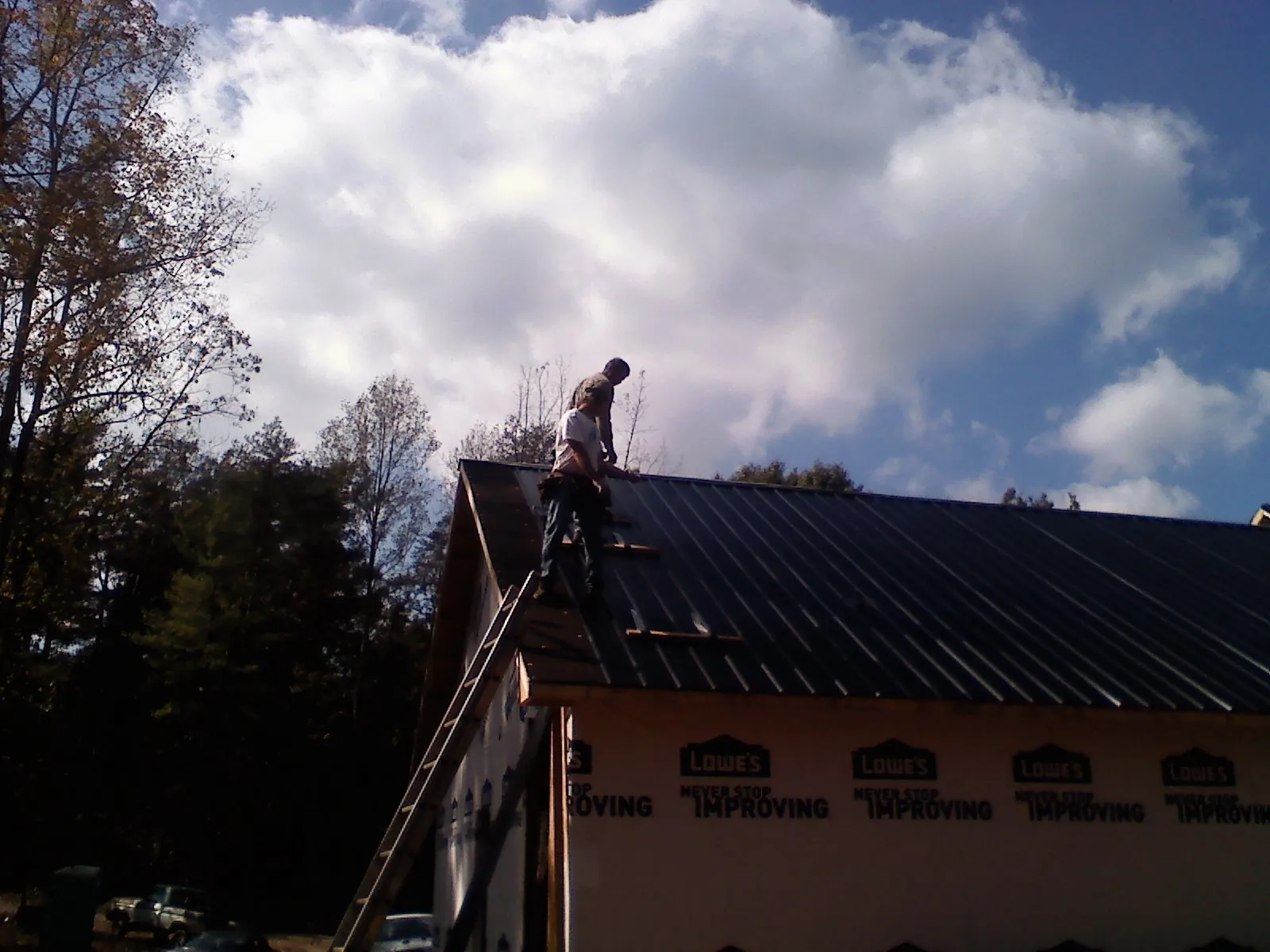 Roofer fastening dark metal panels high against a cloudy sky, from a Roof Inspection job in Selmer