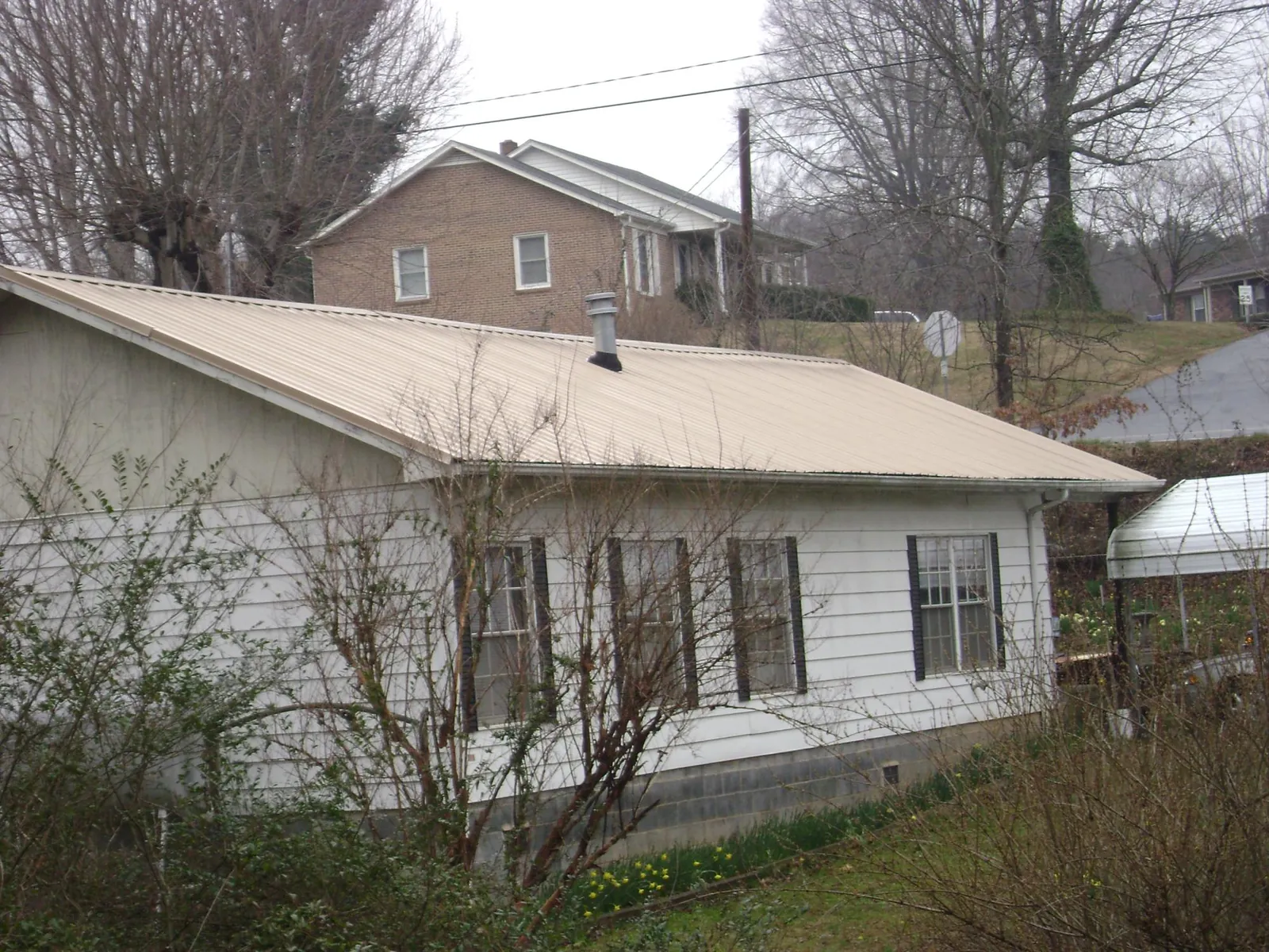 Tan metal roof on a white sided house set into a hillside — Commercial Roofing by Roofing Brothers in Selmer
